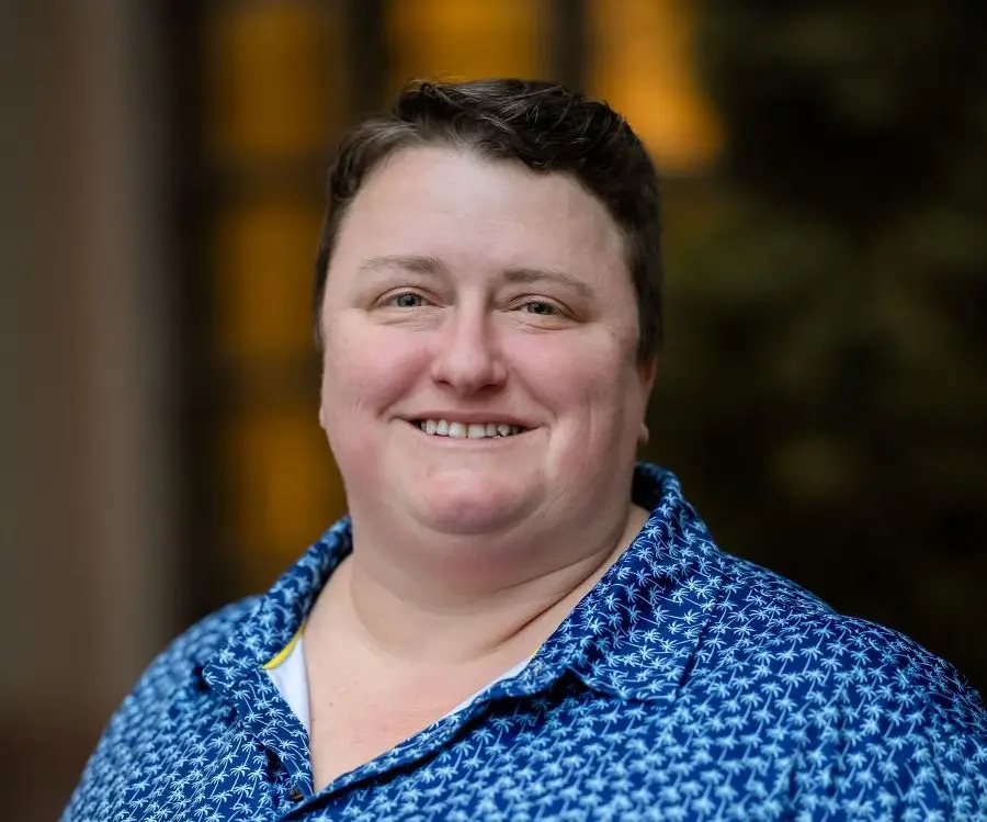 Headshot of person wearing a blue collared shirt with a white palm tree pattern.