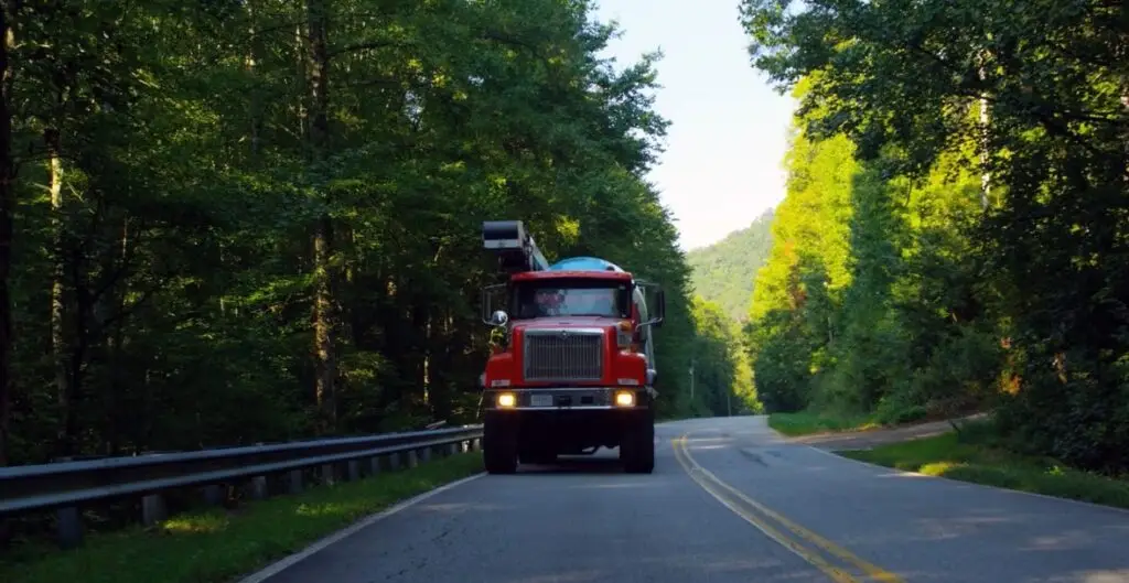 Front view of concrete mixer truck on the road, forest of trees on either side.