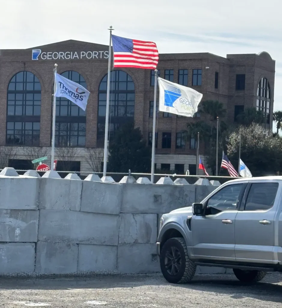 Three flags rise behind a concrete block wall