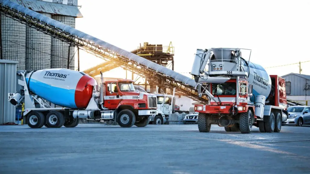 Rear discharge and front discharge concrete mixers in front of a conveyor belt