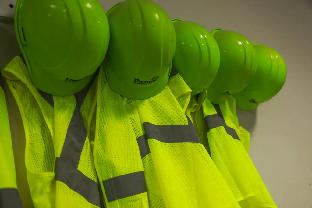A row of bright green hard hats and high-visibility safety vests