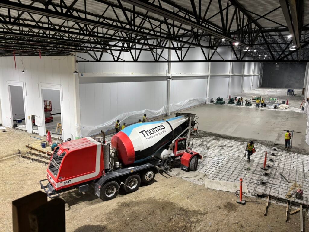 A red, blue, white, and black concrete mixer pouring a concrete floor inside a warehouse