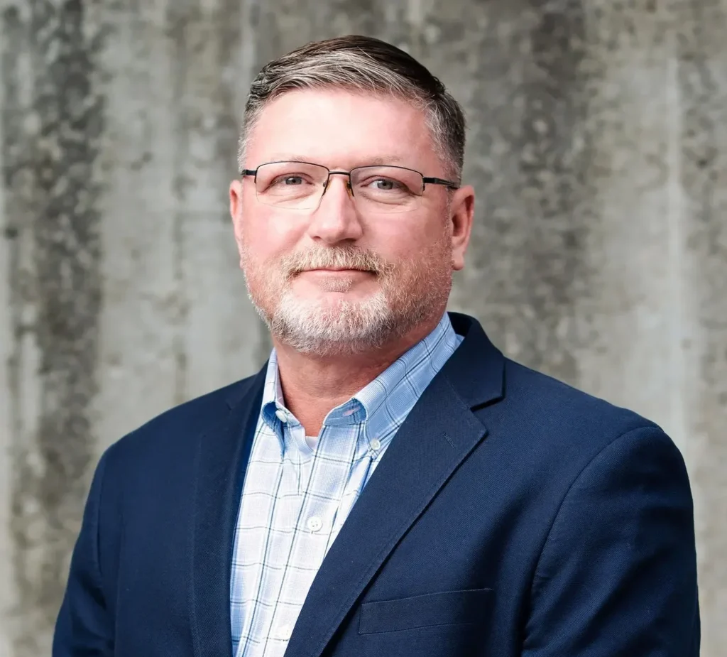 Image of man in glasses and blue blazer in front of gray background