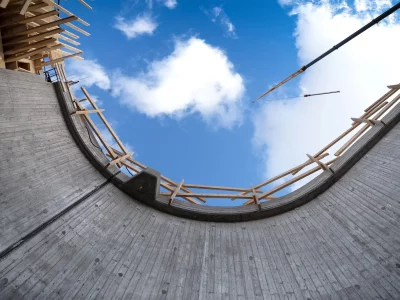 View of sky from the ground with concrete wall around the edge. Crane lowering wood down into the concrete formation.